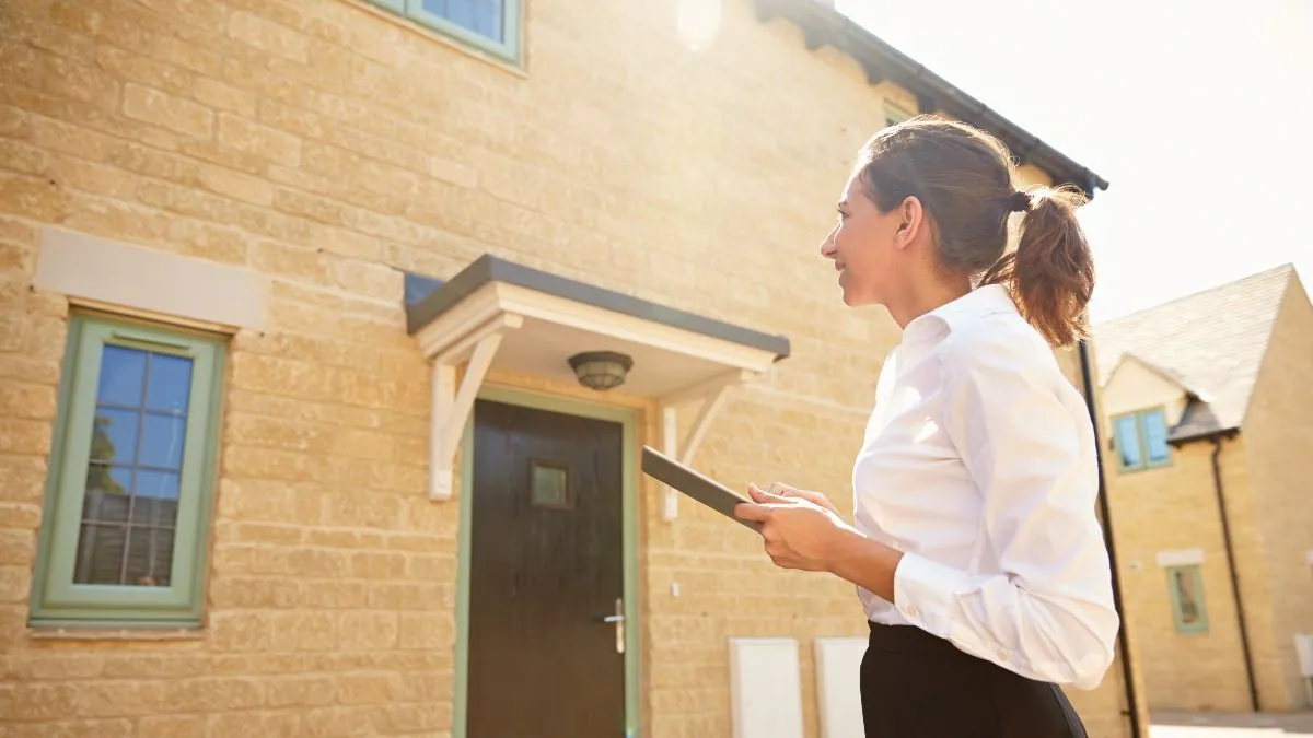 A planning officer outside a Cotswold-stone home reviewing the application on a tablet