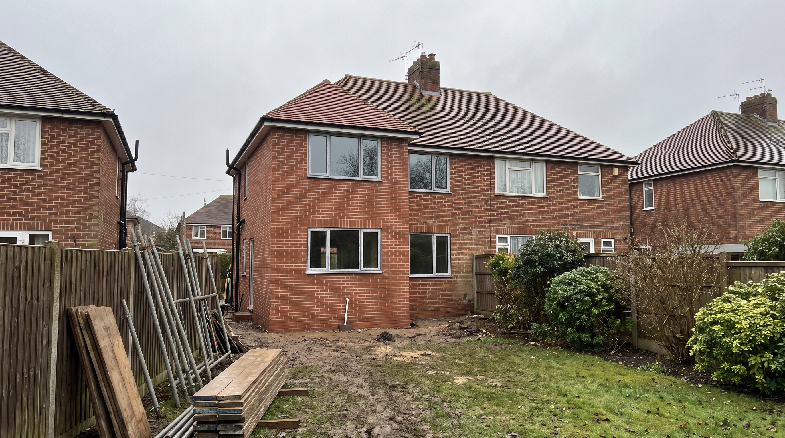 Completed two-storey extension on a semi-detached house, built in red brick with a tiled roof to match the original home, with the rear garden awaiting landscaping.