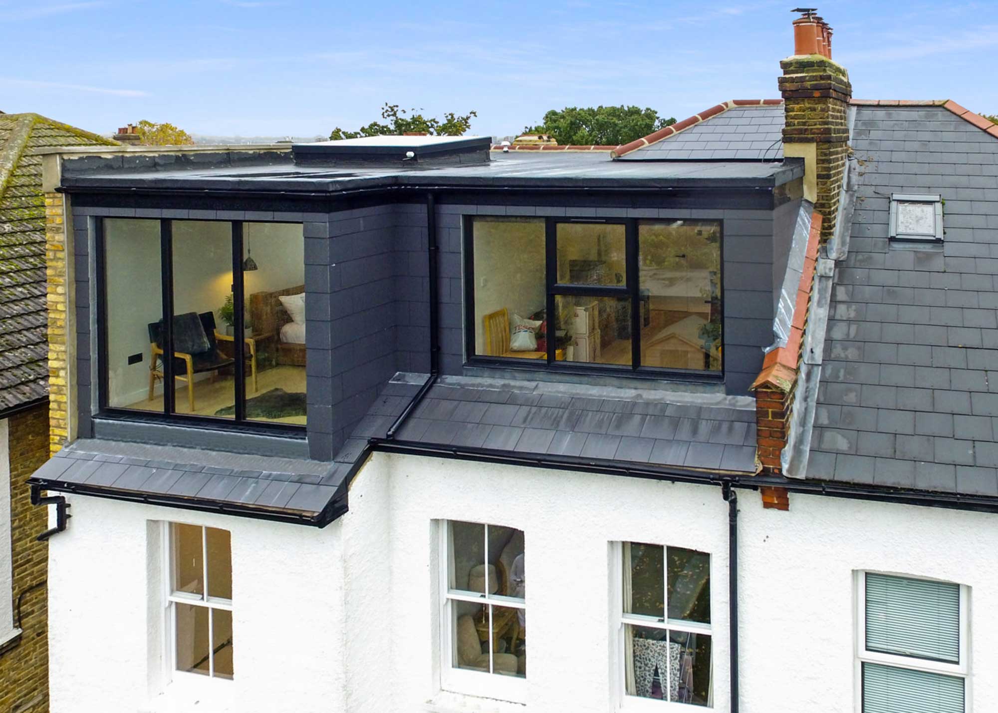 Modern L-shaped rear dormer loft conversion with large picture windows, clad in dark grey slate-effect tiles, on a Victorian terrace.